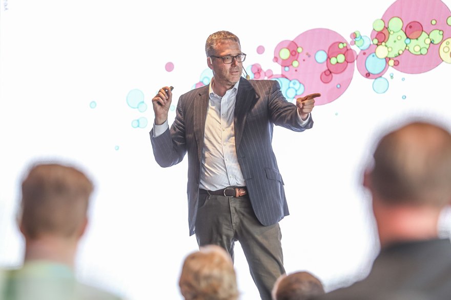 Olof Gränström föreläser på scen framför en publik. Bakom sig har han en storbildsskärm med bubblor på.